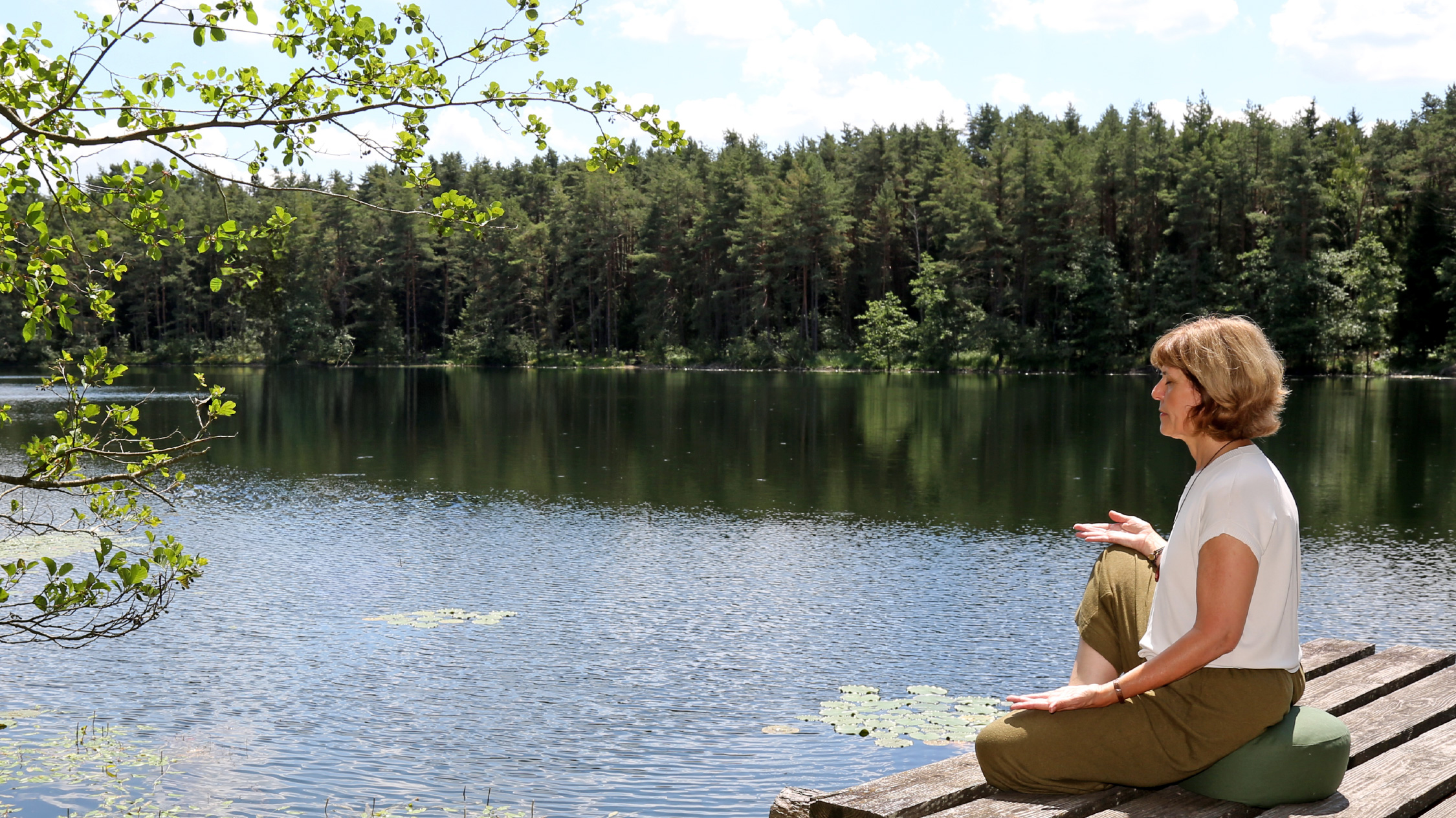 Stefanie Grzeski-Ruf auf einem Steg im Meditationssitz an einem See